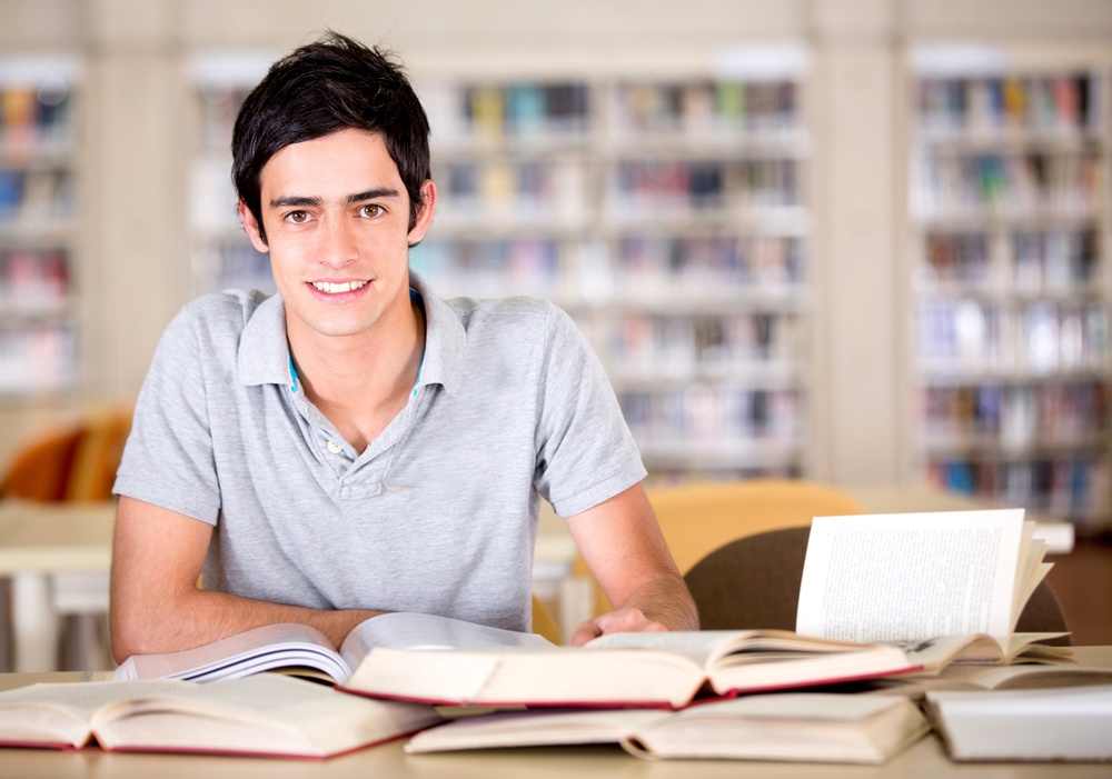 Happy university student at the library reading books